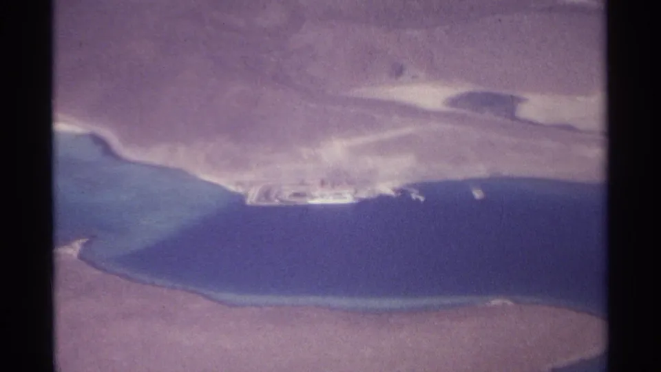 1974 La Paz-area aerial view with deep blue water, sandy shoreline and a distant pale structure along the coast.