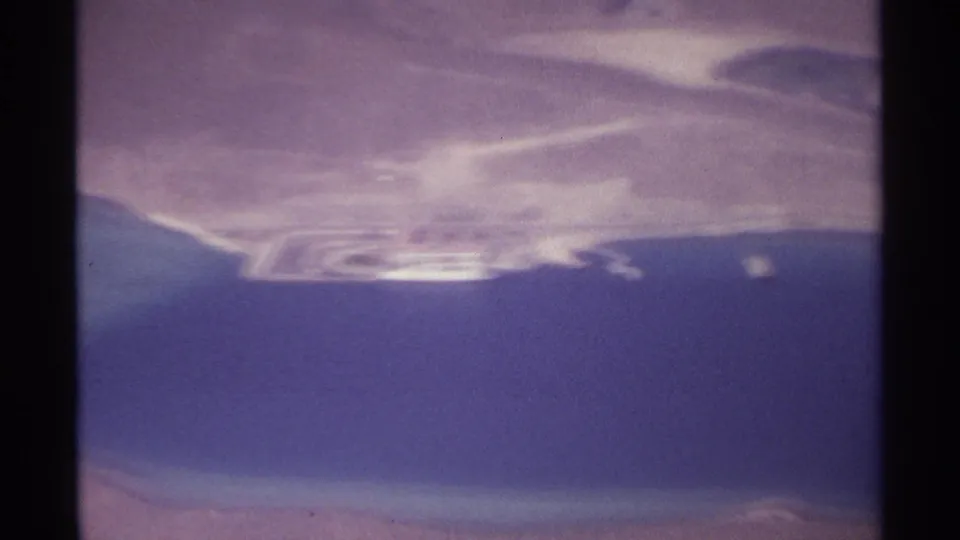 Soft 8mm aerial frame near La Paz showing blue water, pale sandy coast and a blurred white feature along the shoreline.