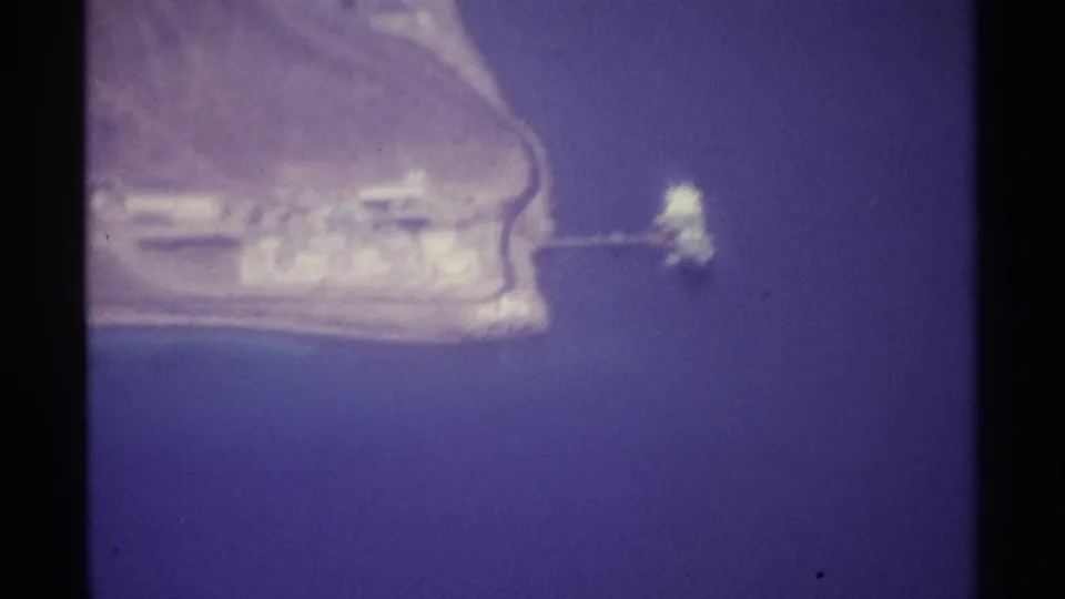 1974 La Paz aerial frame with blue water, a pale waterfront edge, low structures, and a narrow pier-like feature extending offshore.