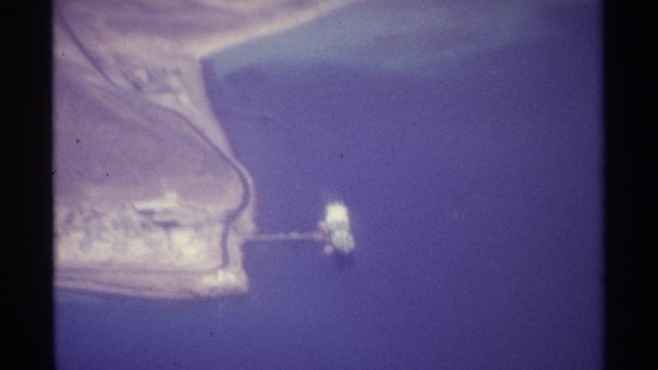 Aerial view of a pale coastline, blue water, dry land, and dark film borders.