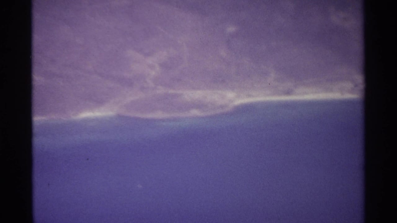 Purple-tinted aerial view of ocean, horizon, and a faint shoreline.
