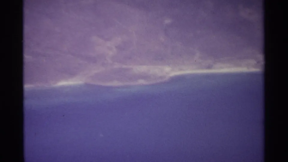 1974 8mm aerial view over La Paz, Mexico, showing blue water, distant shoreline, and soft horizon through purple-tinted film.