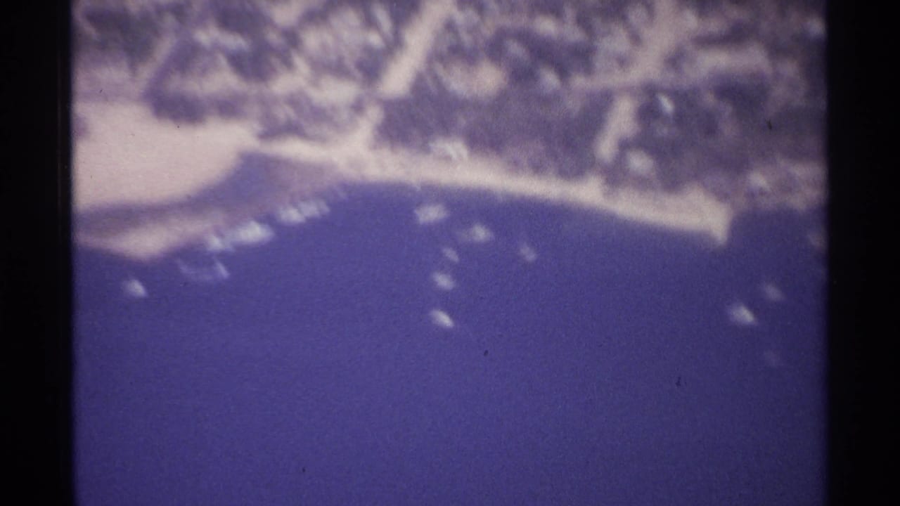 Aerial view of a curved shoreline with small boats offshore.