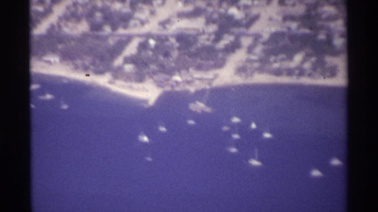 Aerial view of a curved shoreline with small boats scattered across blue water.