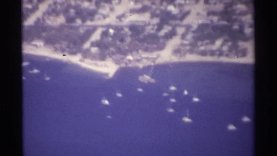 1974 La Paz, Mexico aerial 8mm frame showing a bay, curved coast, anchored boats, and low-rise waterfront buildings.