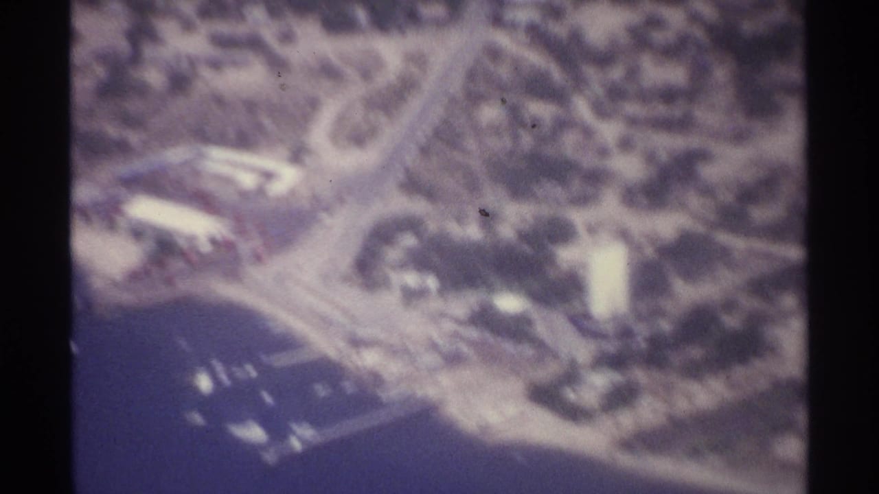 Aerial coastline view with roads, shoreline buildings, and small boats in the water.