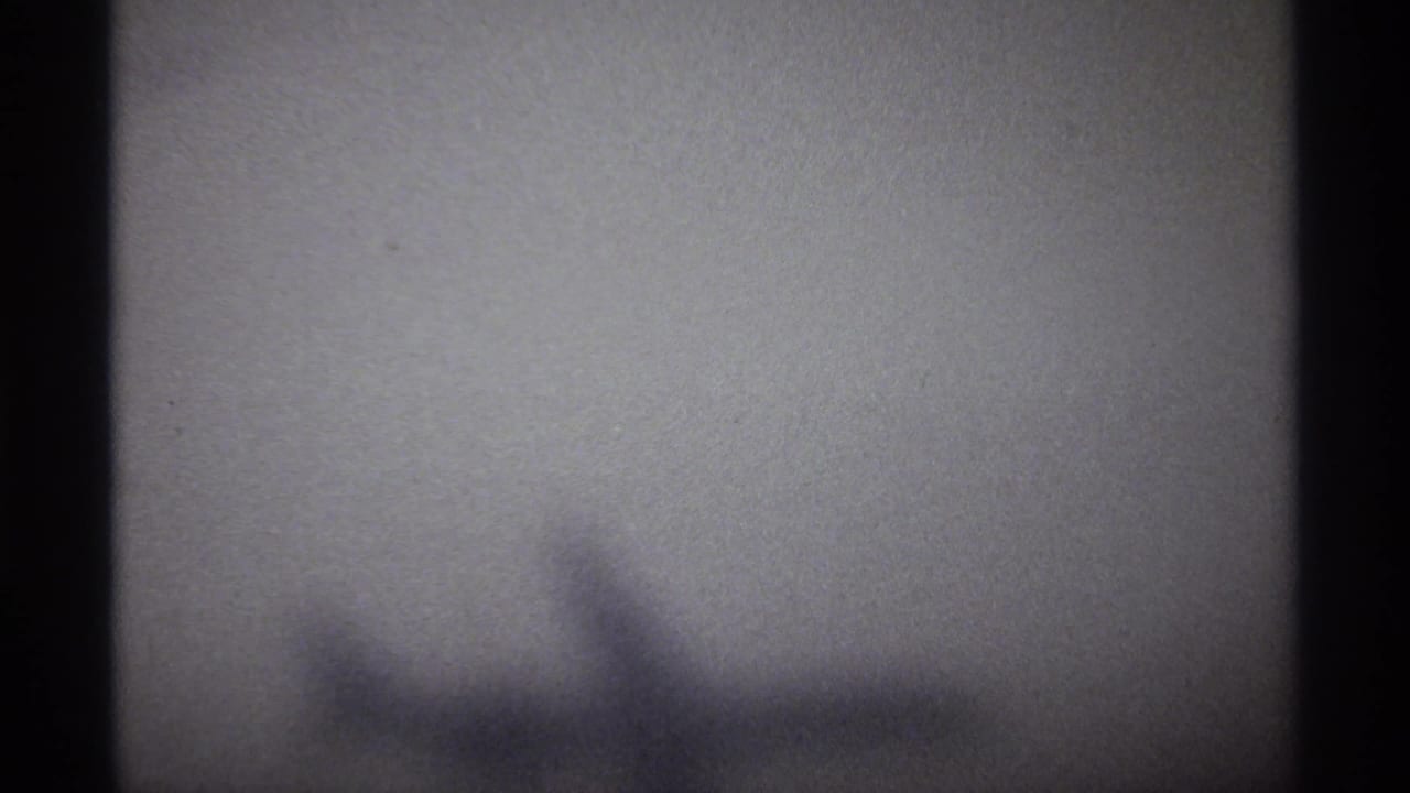 Soft, grainy 1974 8mm frame from La Paz travel footage showing a washed-out sky and indistinct aircraft-wing-like shape.