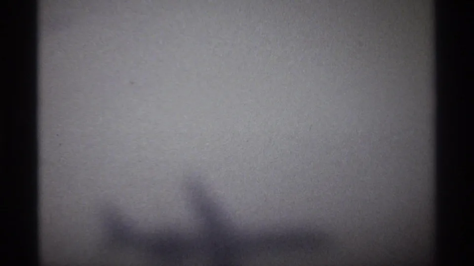 Soft, grainy 1974 8mm frame from La Paz travel footage showing a washed-out sky and indistinct aircraft-wing-like shape.