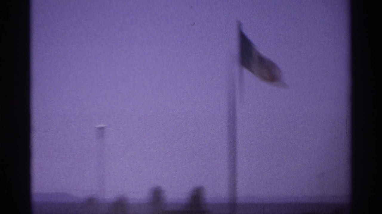 Flag on a pole against a hazy sky with indistinct horizon shapes.