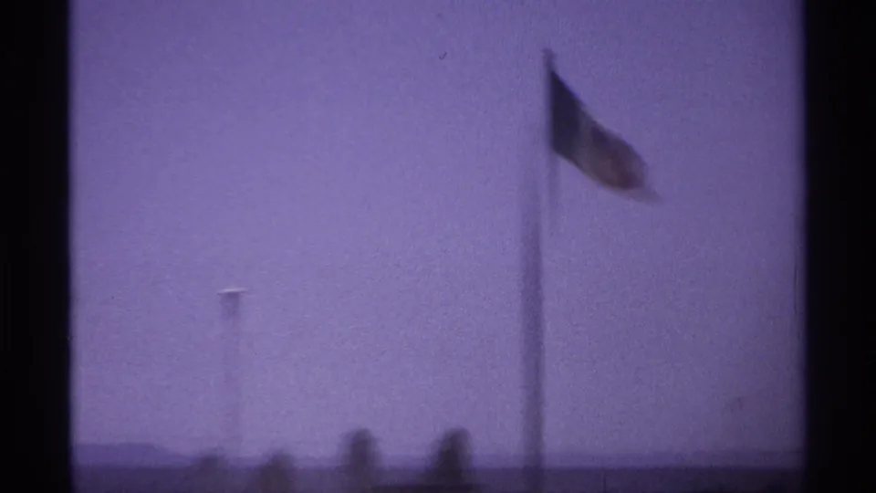 Blurry 1974 La Paz, Mexico frame showing a flag on a pole above a soft horizon under a purple-tinted sky.