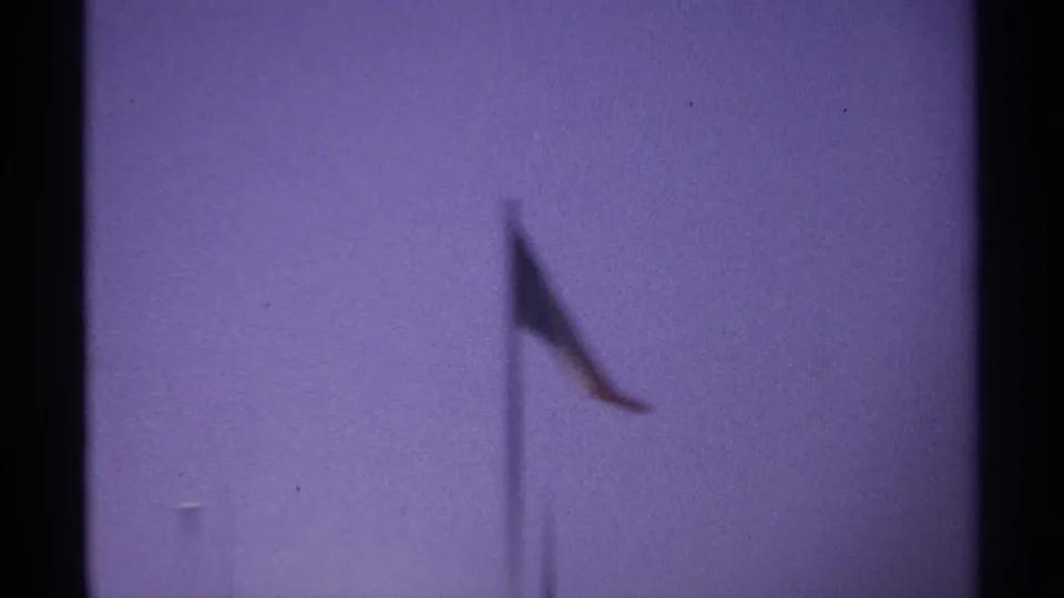 Soft-focus 8mm frame from the 1974 La Paz clip with a flag and pole drifting through a purple sky.