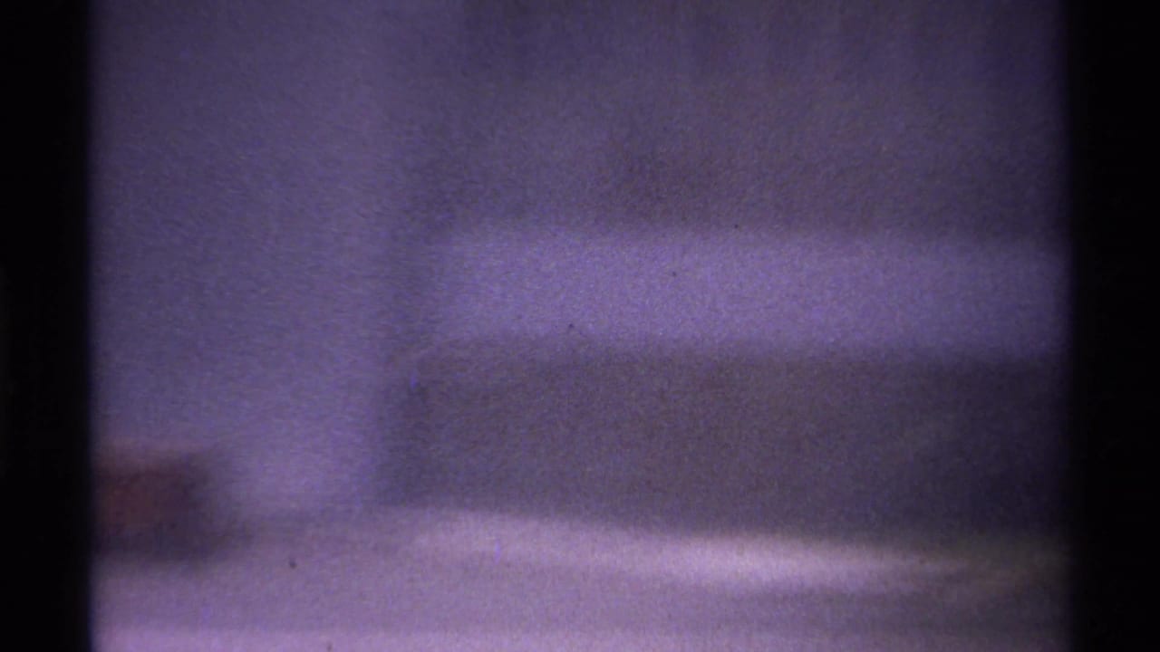 1974 La Paz, Mexico home-movie frame showing a soft, grainy building facade partly obscured by dark vertical bars.
