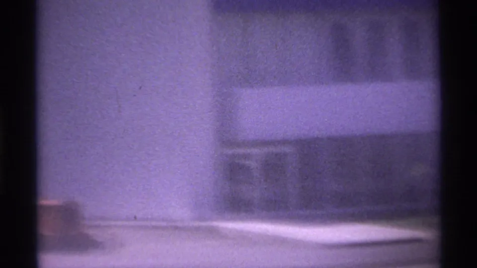 1974 La Paz, Mexico frame showing a soft, purple-tinted facade section with a pale wall, shadowed band, and indistinct sign area.