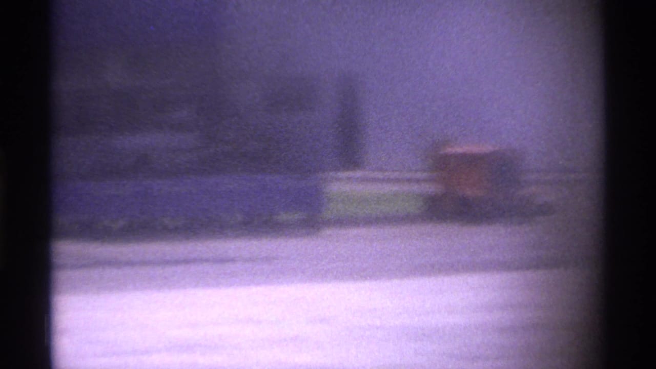 Blurred tarmac view through dark film gate shadows with distant vehicles or ground equipment.