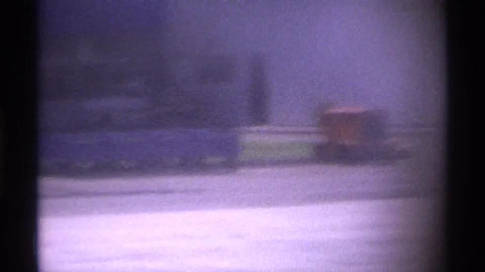 Soft 1974 La Paz airport home-movie frame showing a blurred tarmac view with dark vertical film edges and distant ground activity.