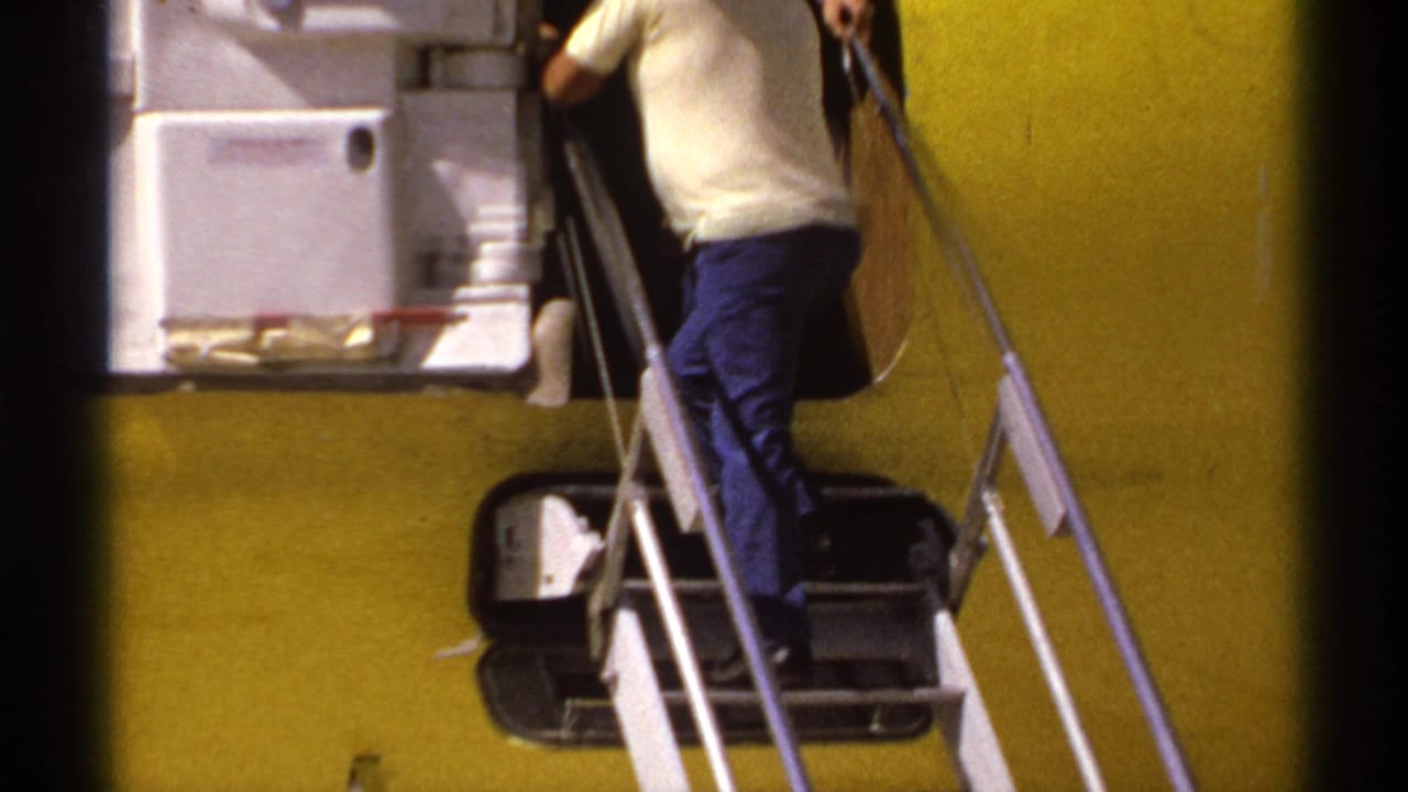 Man in light shirt climbs metal stairs into a yellow aircraft on a tarmac.