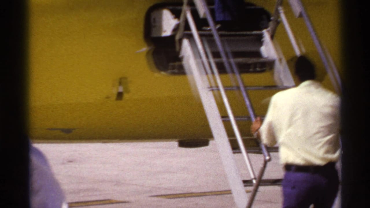 Passenger approaches metal stairs beside a yellow aircraft with dark cabin windows.