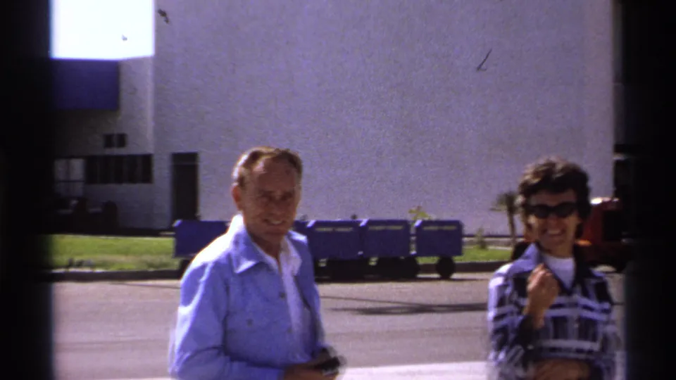In La Paz, Mexico, a man in a light blue shirt and a woman in sunglasses stand outside a modern building in 1974 footage.