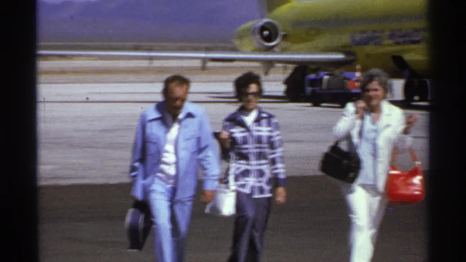 Three adult travelers walk toward the camera on a La Paz airport tarmac with a yellow aircraft in the background.