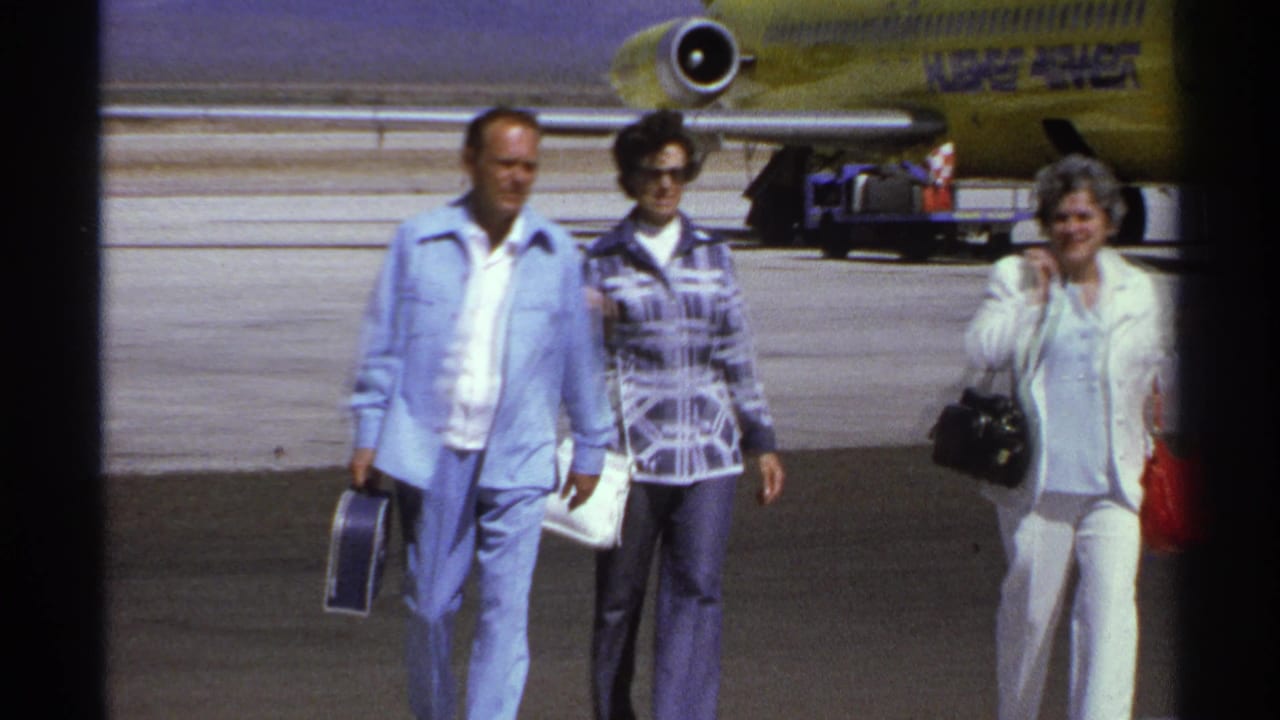 Three adults walk across an airport tarmac with a yellow jet behind them.