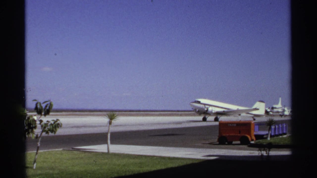 1974 La Paz, Mexico airport view with a white propeller airliner on the runway, seen through dark window framing.