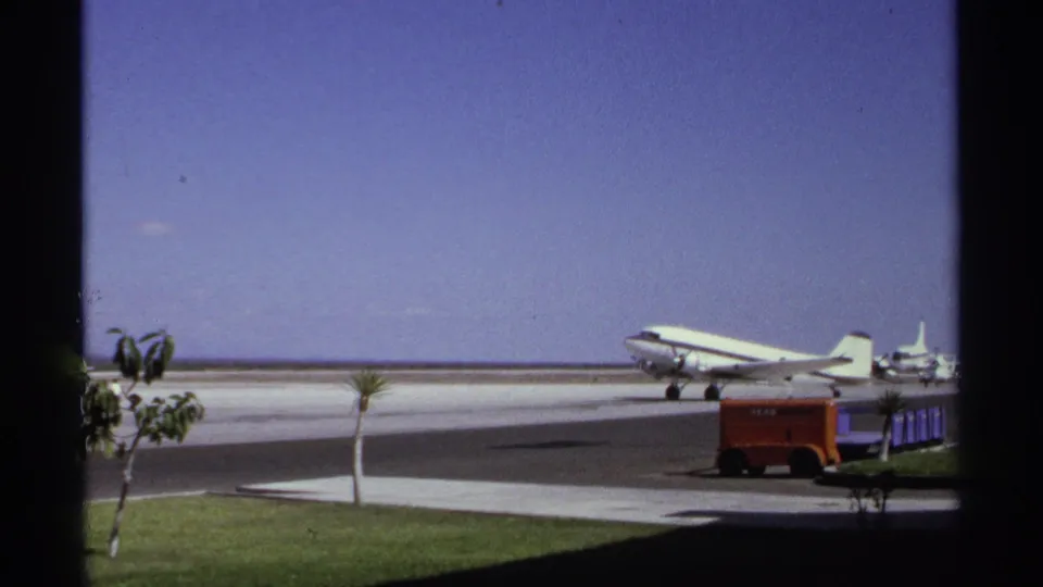 1974 La Paz, Mexico airport view with a white propeller airliner on the runway, seen through dark window framing.