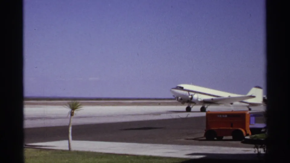 White propeller airliner taxiing at the La Paz airport in 1974, with palm trees and Aero Mexico ground equipment visible.