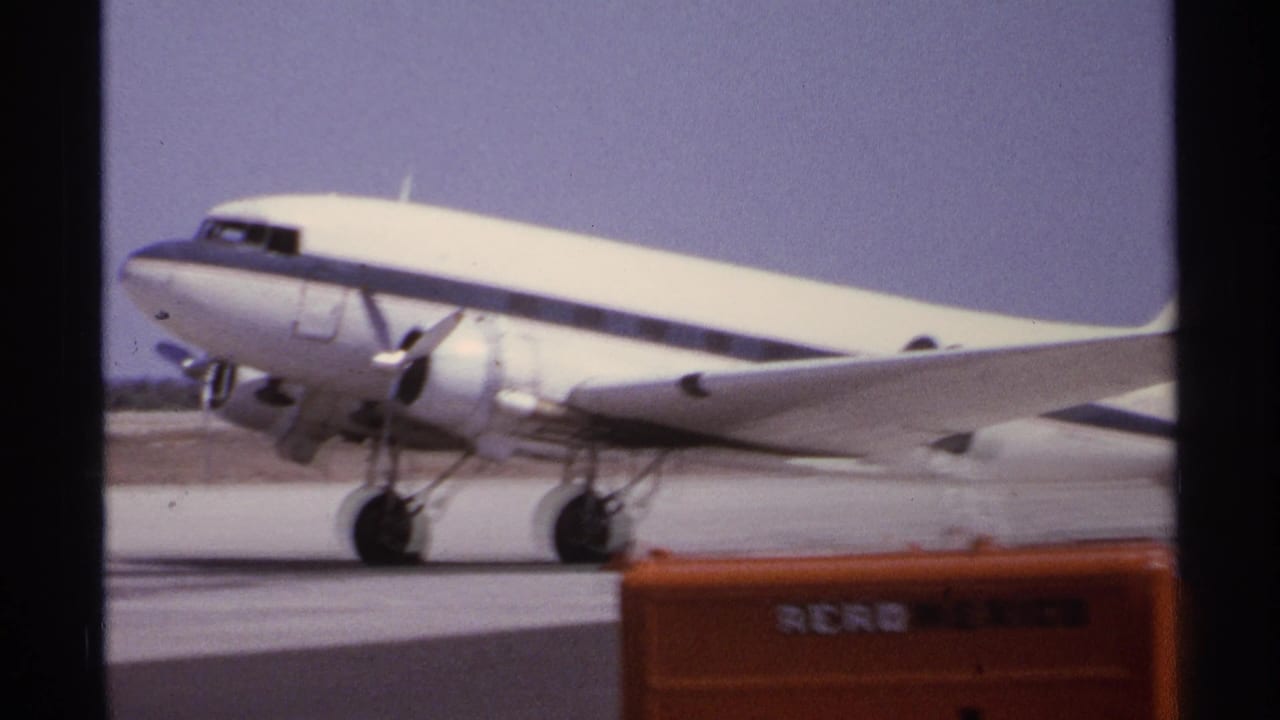 1974 La Paz, Mexico airport footage showing a white-and-blue twin-prop aircraft moving across the tarmac with orange ground equipment in front.