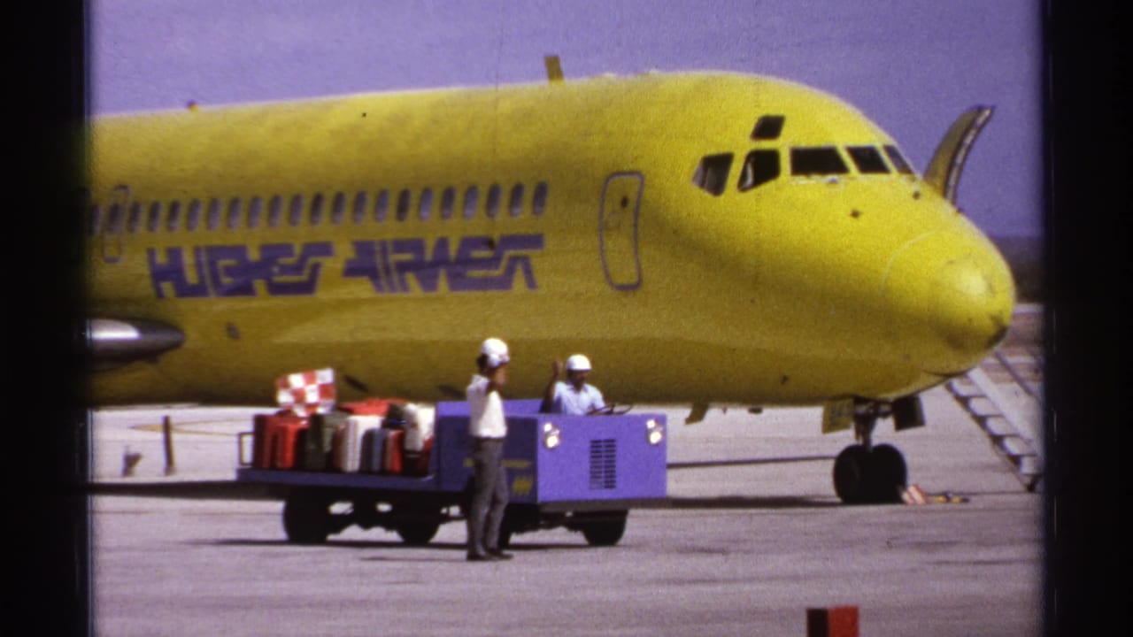 Ground crew with a luggage cart positioned near the nose of a yellow aircraft.