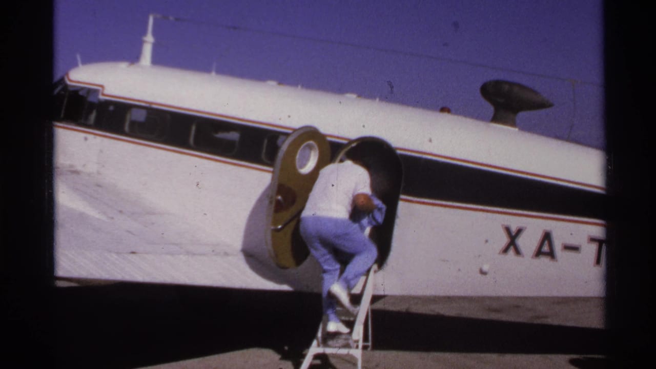 A man climbs the stairs into the oval doorway of a small white aircraft.