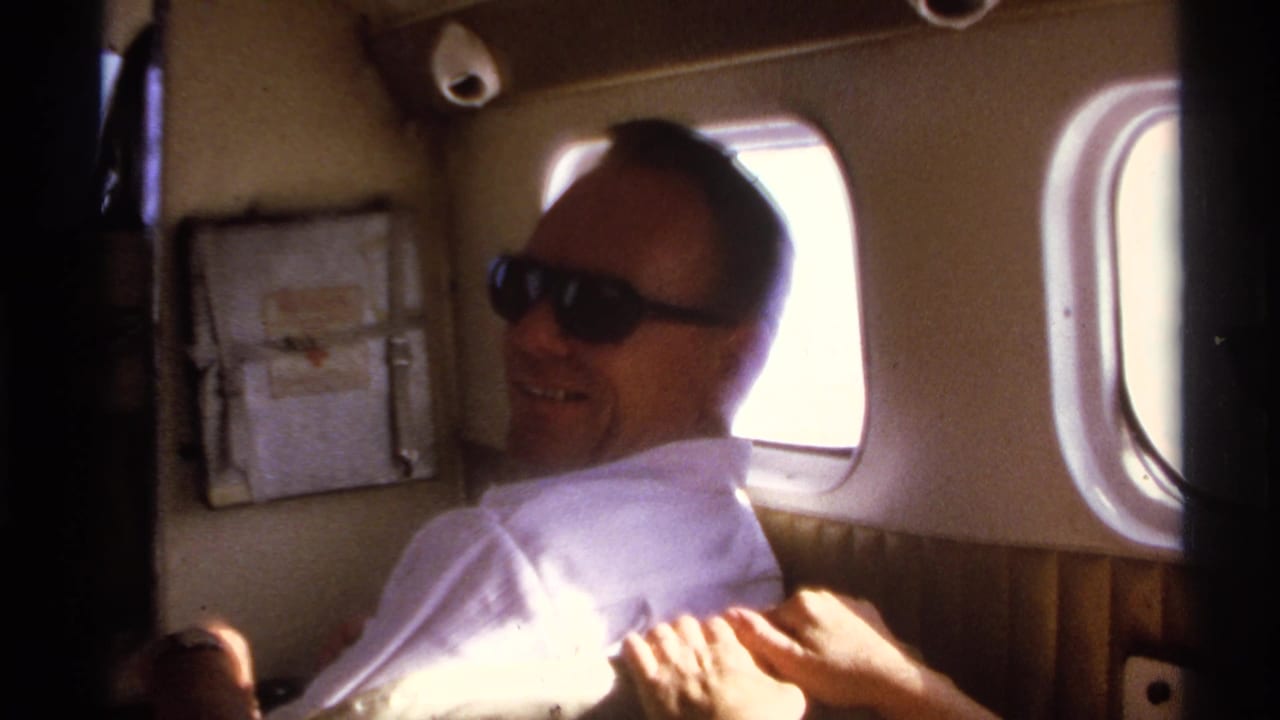 Man in sunglasses smiles from a seat inside a small aircraft cabin.