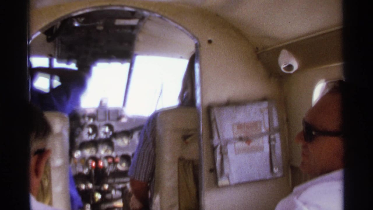 Men seated inside a small aircraft cockpit area with instrument panel ahead.