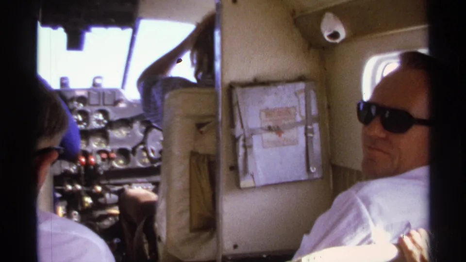 1974 La Paz aircraft cabin frame with a man in sunglasses facing the camera while the cockpit and cabin wall remain visible.
