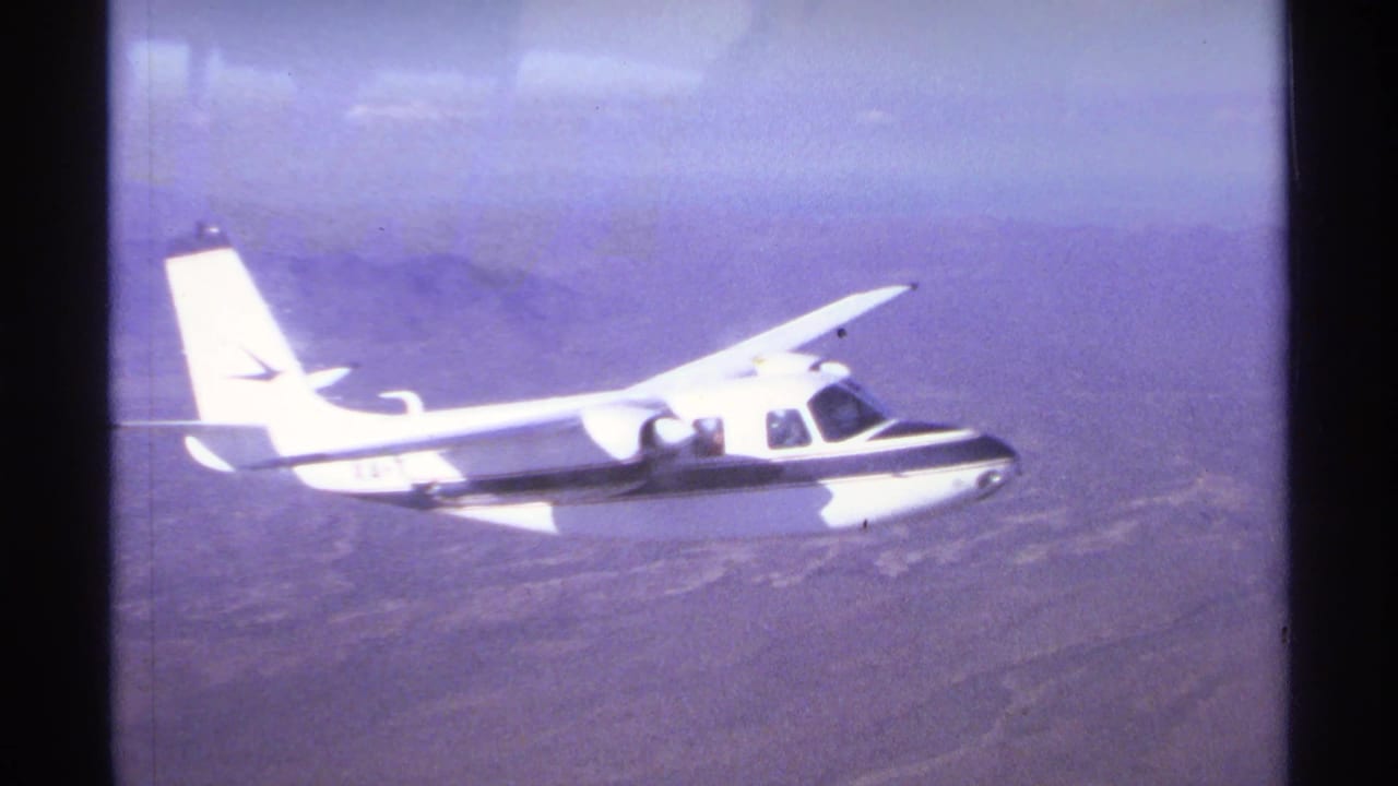 White single-engine aircraft flying over hazy arid terrain.
