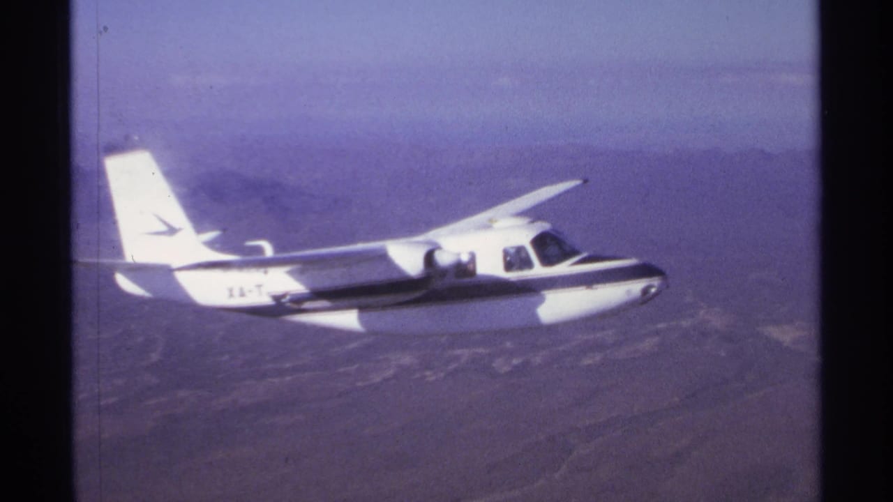 Small white aircraft in side view above distant hills.
