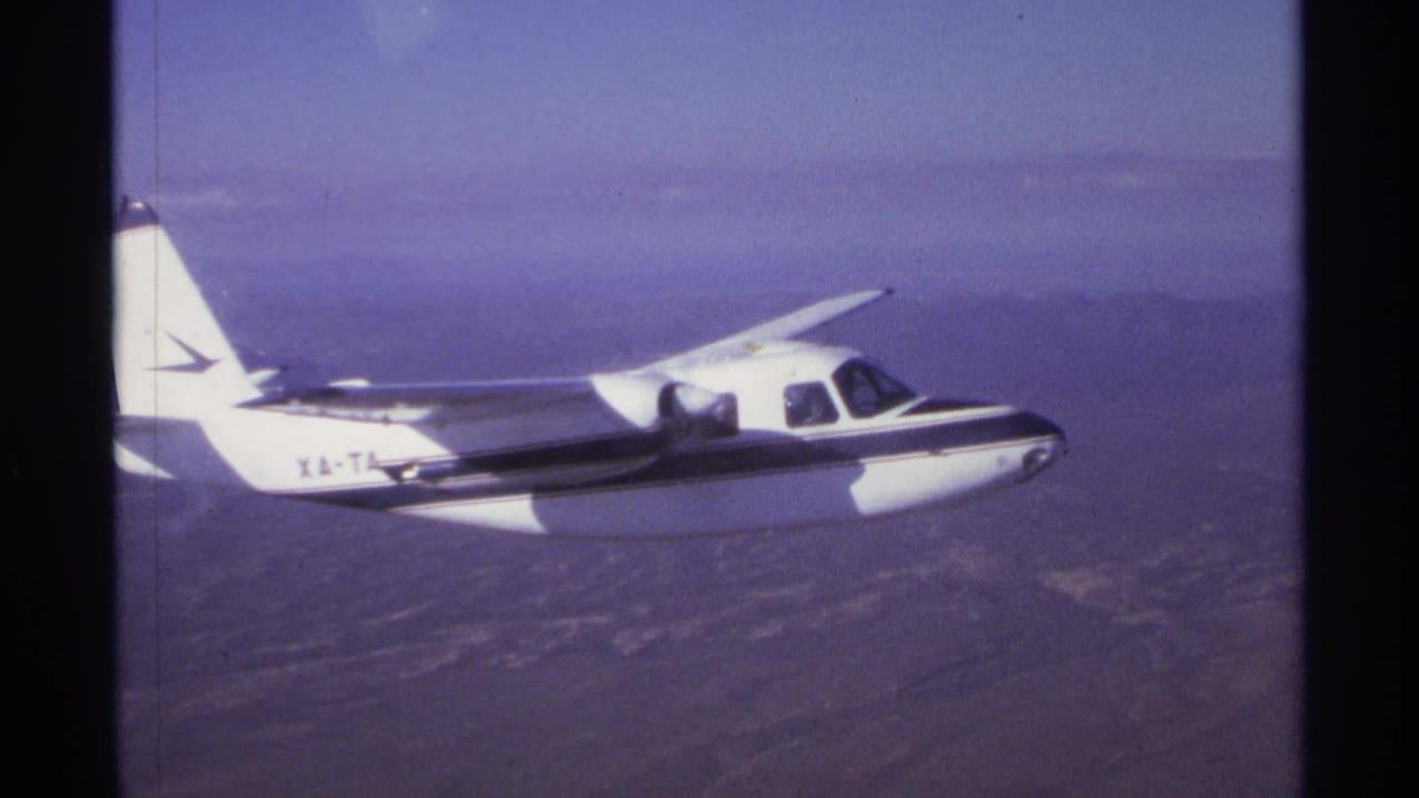 Small white propeller plane flying over hazy arid terrain.