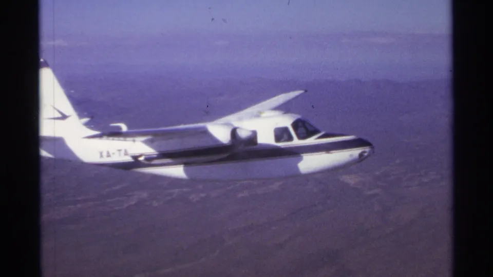 Small aircraft marked with visible lettering flies steadily over the La Paz area in this 1974 8mm frame.