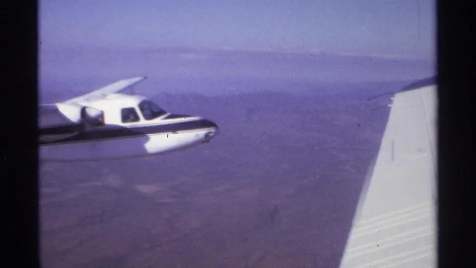 1974 8mm frame from La Paz showing a small propeller plane near the filming aircraft's wing over hazy arid ground.