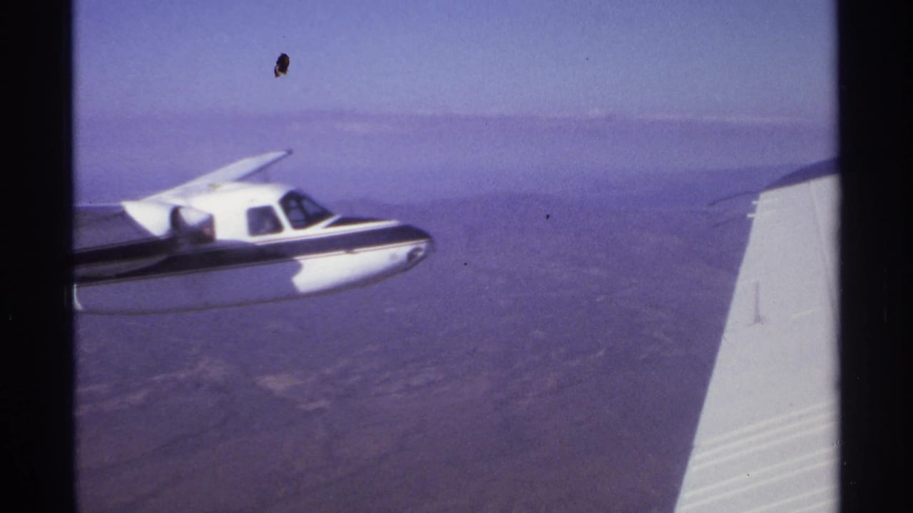 Small white and dark propeller plane flying beside another aircraft over arid terrain.