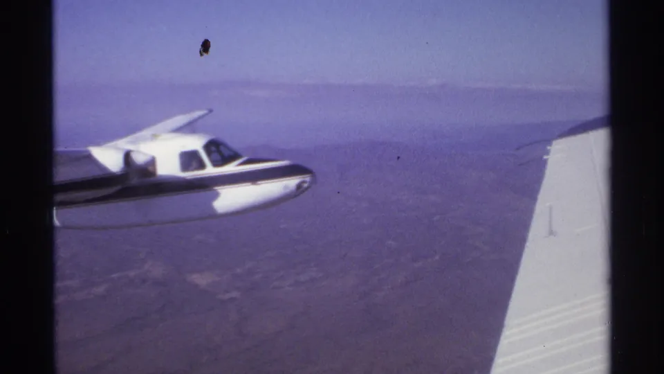 1974 8mm frame near La Paz, Mexico, showing a small propeller plane flying beside the filming aircraft over hazy dry land.