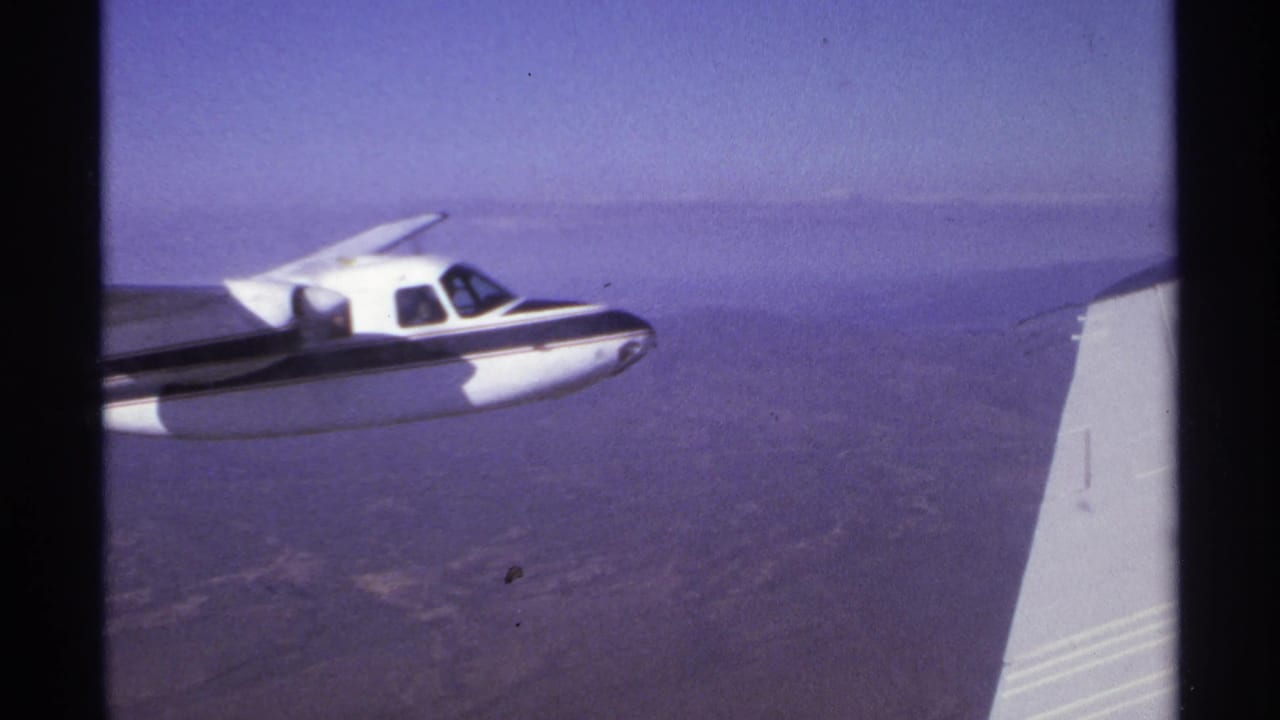 Small propeller plane in profile with a wingtip from the filming aircraft at right.