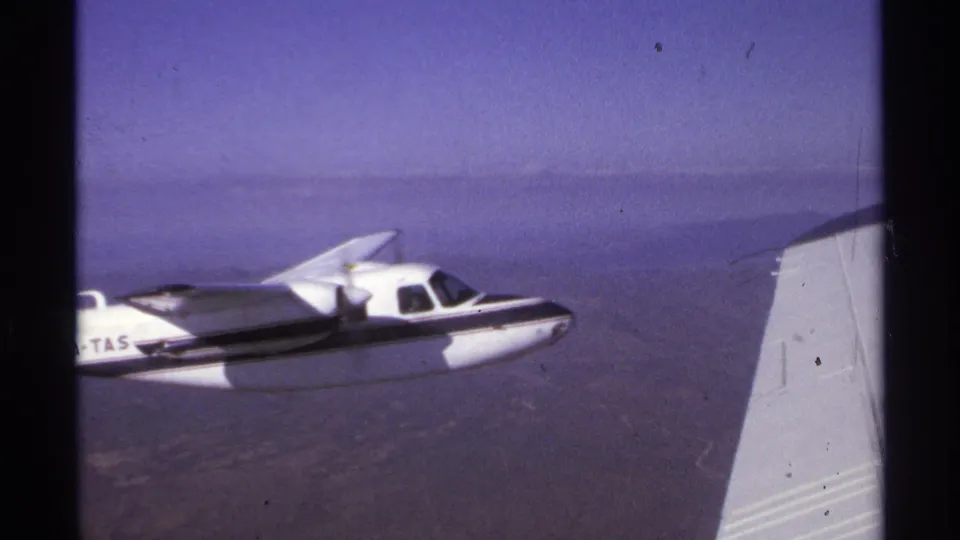 Small white aircraft with visible XA-TAS marking flies past the filming aircraft wing in 1974 La Paz, Mexico footage.
