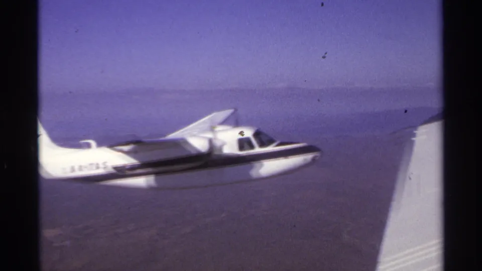 Final 8mm frame shows the small white aircraft flying steadily near the filming aircraft wing over hazy La Paz water.