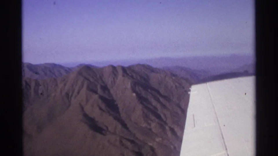 1974 8mm aerial view near La Paz, Mexico with the filming aircraft wing over dry mountain ridges and purple sky.