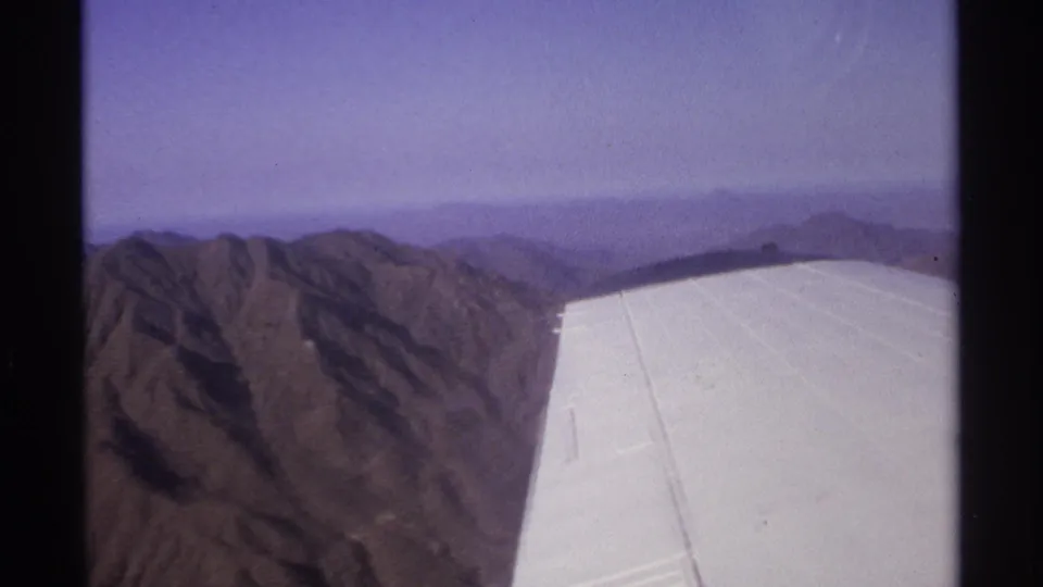 Aerial 8mm frame from 1974 near La Paz, Mexico showing the plane wing over rugged brown mountains.