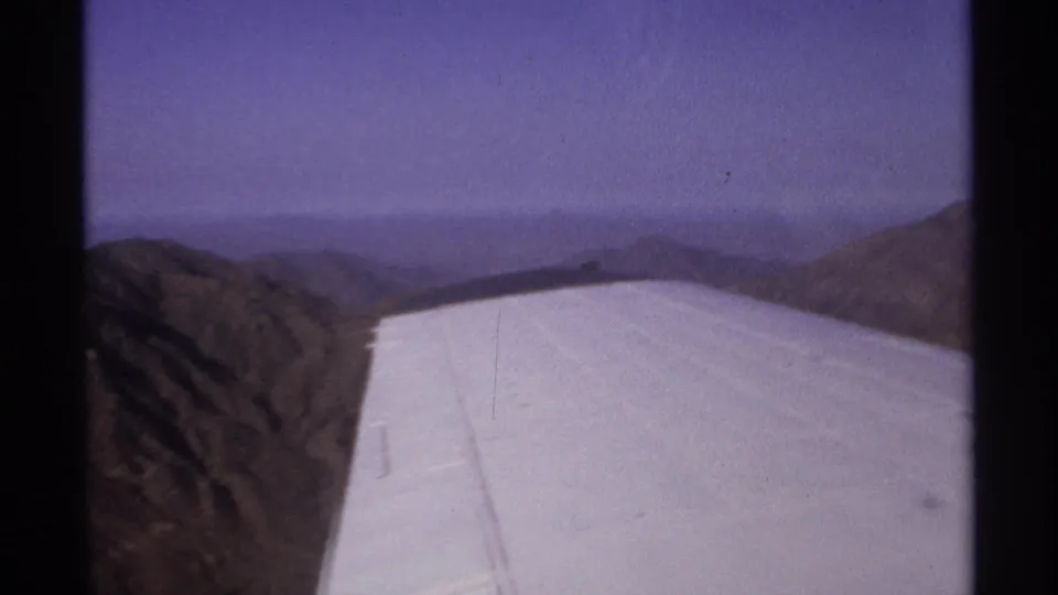 1974 8mm aerial view near La Paz, Mexico with a white aircraft wing filling the foreground over mountain terrain.