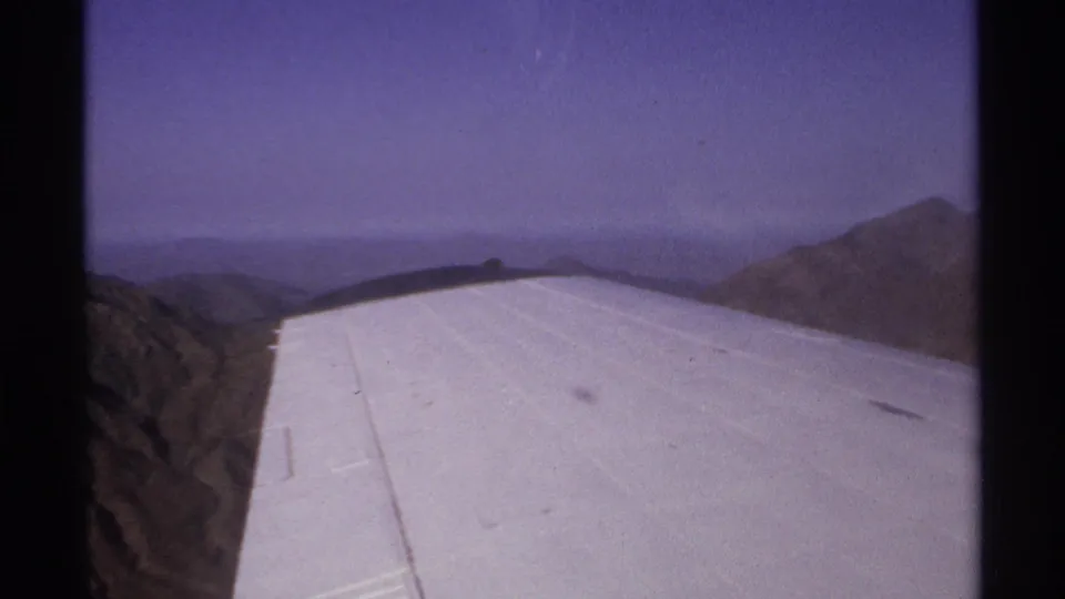 1974 8mm travel view from a plane over mountainous terrain near La Paz, Mexico, with the wing filling the foreground.
