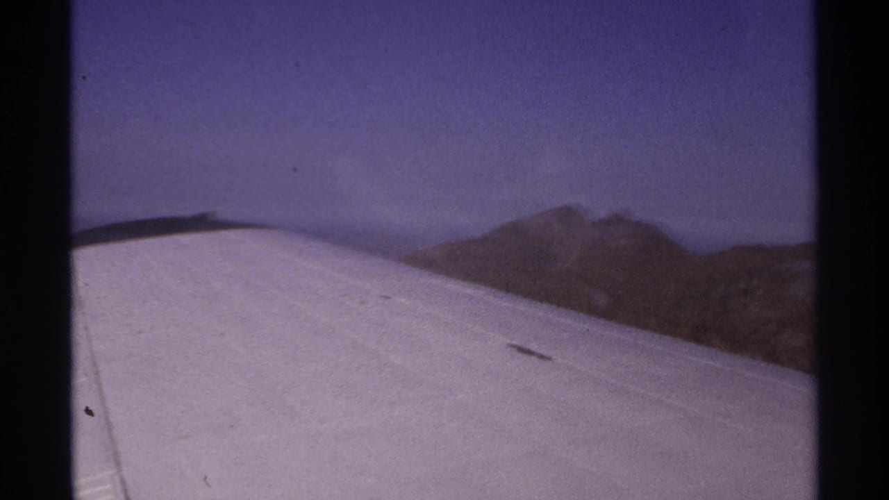 Airplane wing crossing the foreground with mountains beyond under a hazy sky.