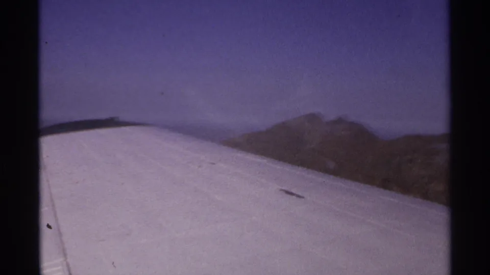 Passenger-window view from an aircraft wing over arid mountain ridges in 1974 La Paz, Mexico travel footage.