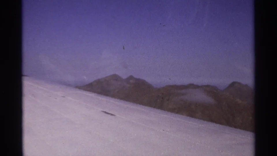 Grainy 8mm aerial view of a white aircraft wing with jagged mountain peaks in the distance near La Paz, Mexico.